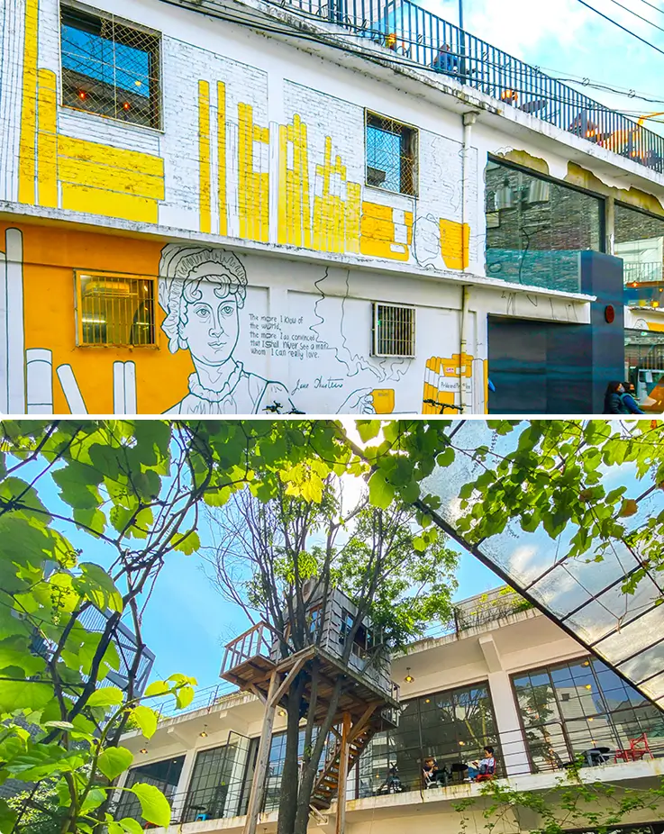 Colorful mural-covered building beside a leafy rooftop cafe with treehouse seating nearby.